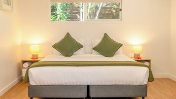 A neatly made bed with green pillows, two bedside lamps, and a window with a view of greenery.