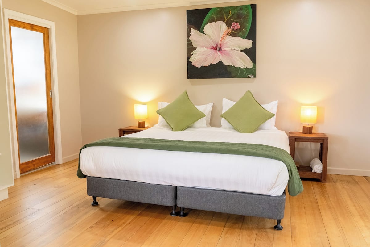 Ein Schlafzimmer mit einem Bett, zwei Nachttischen, einer grünen Tagesdecke und einem Blumenbild an der Wand.