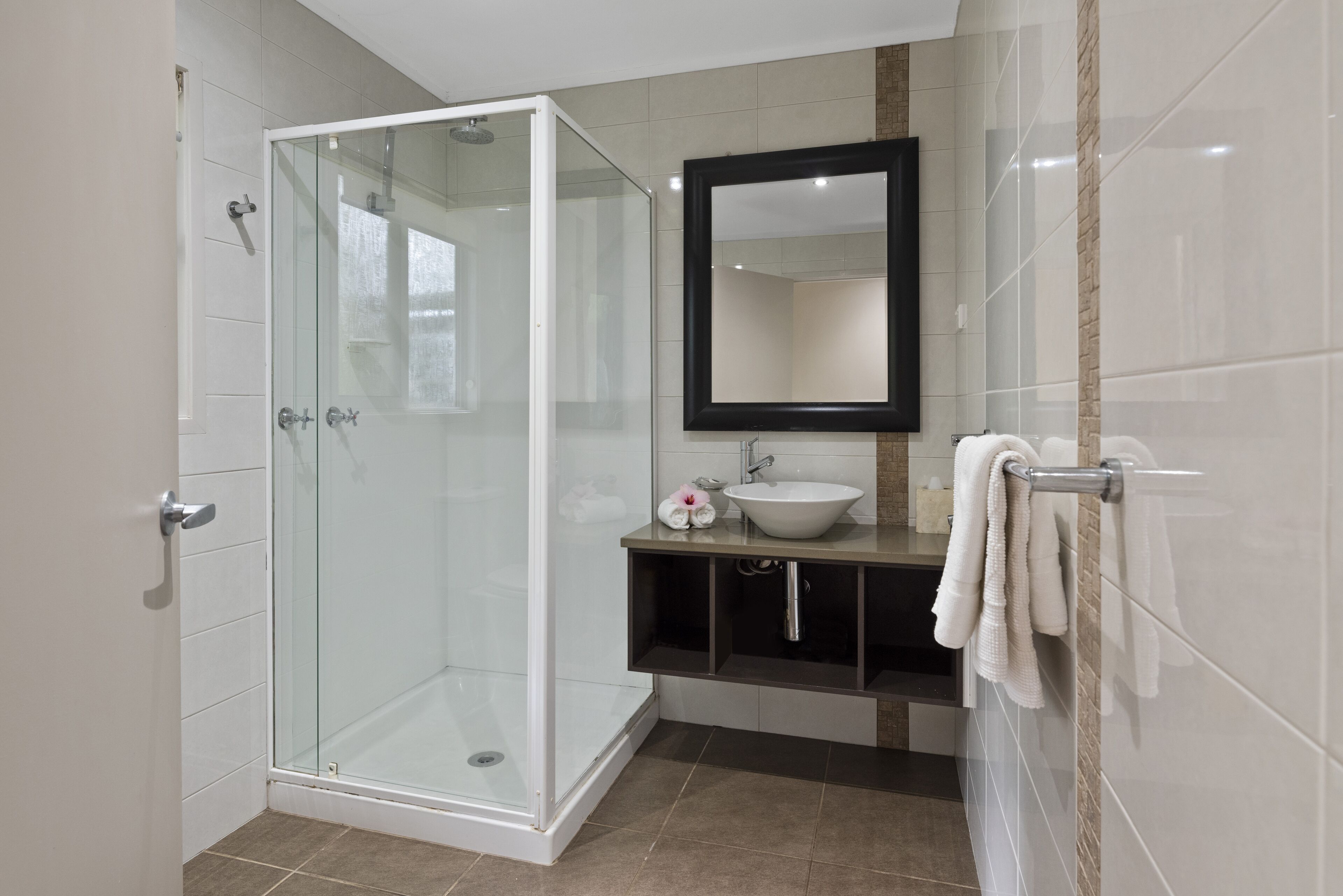 A modern bathroom with a glass-enclosed shower, a sink, a mirror, and a towel rack.