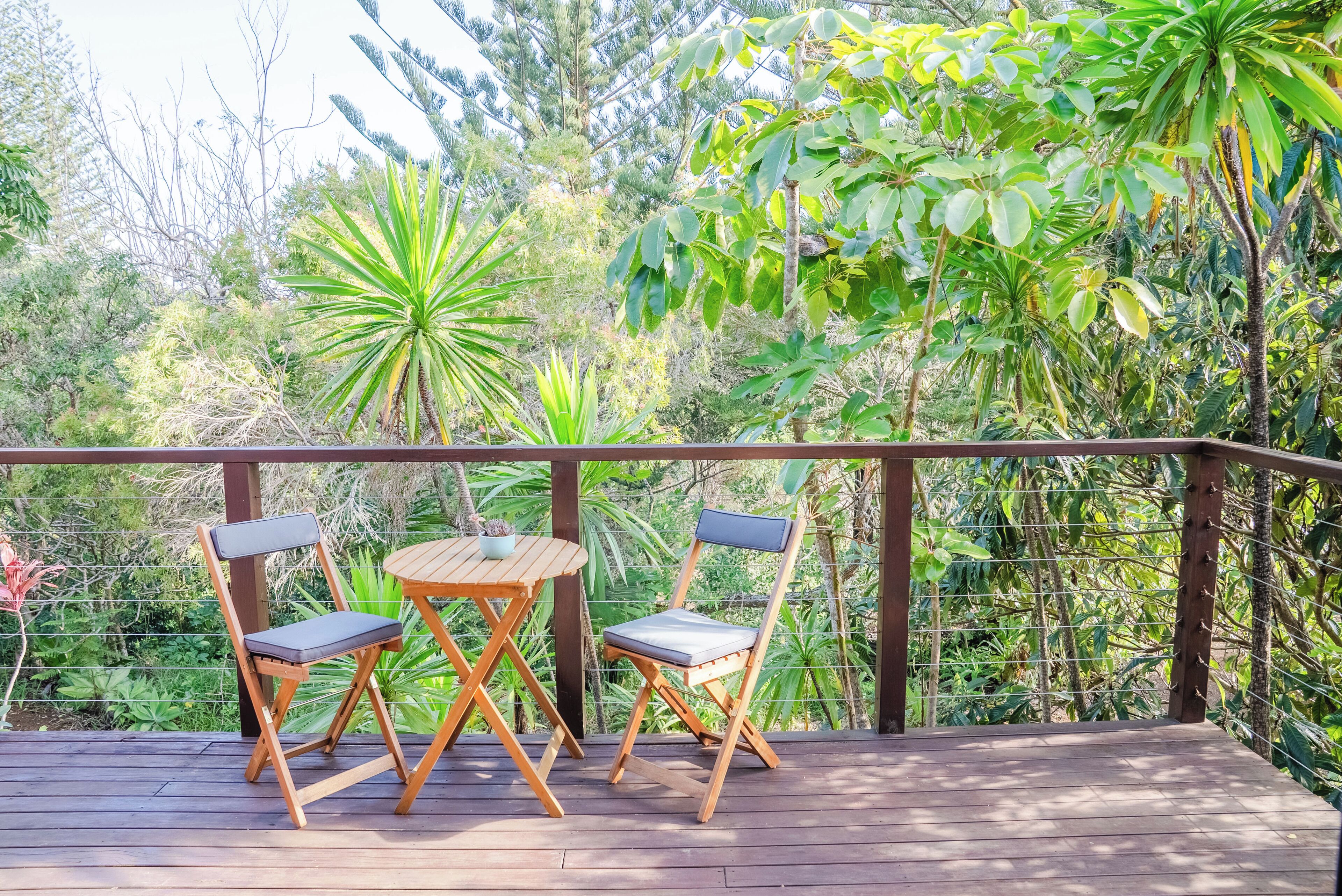 Una terraza de madera con dos sillas y una mesa, rodeada de exuberante vegetación y árboles.