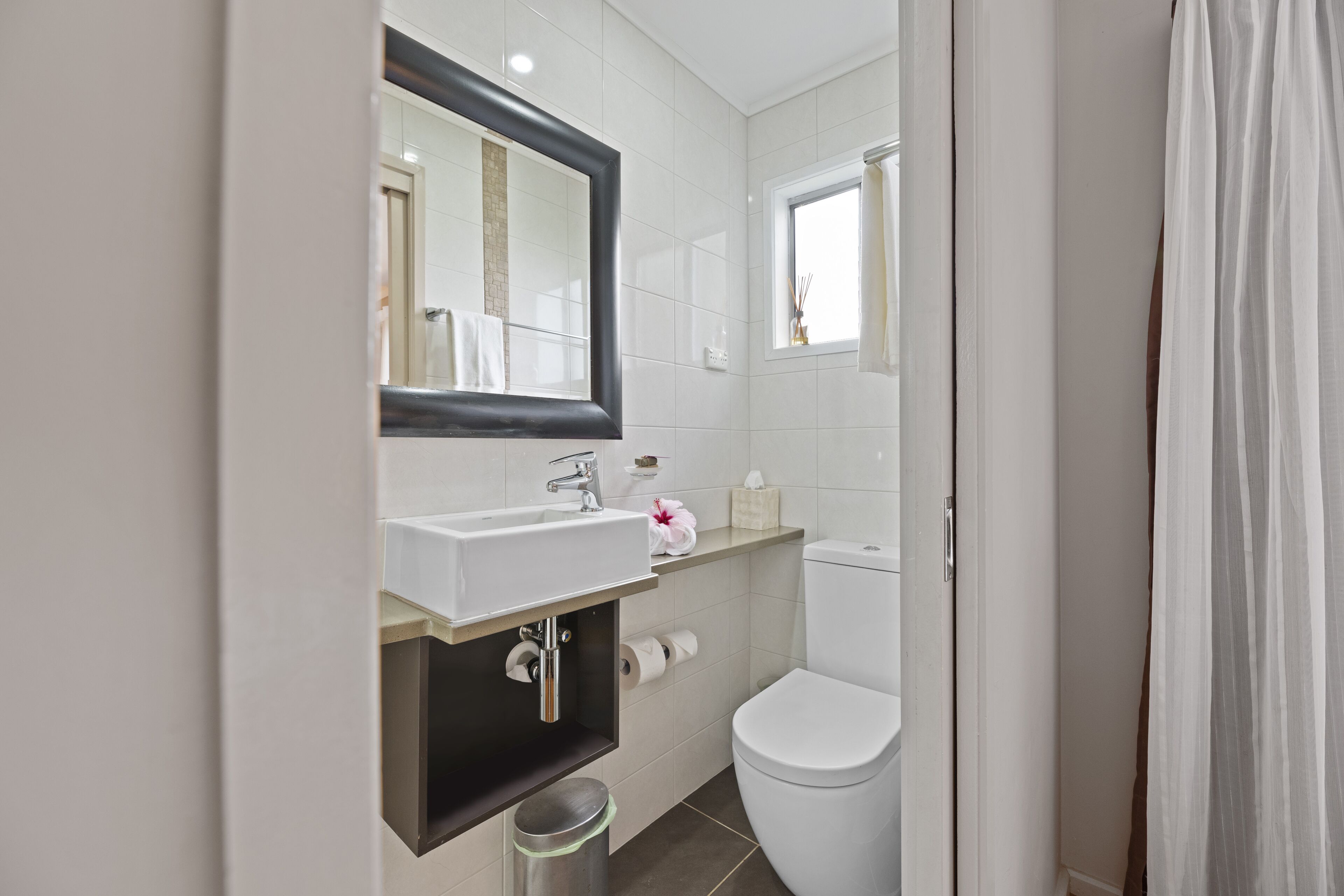 Un baño moderno con lavamanos, espejo y retrete blancos.