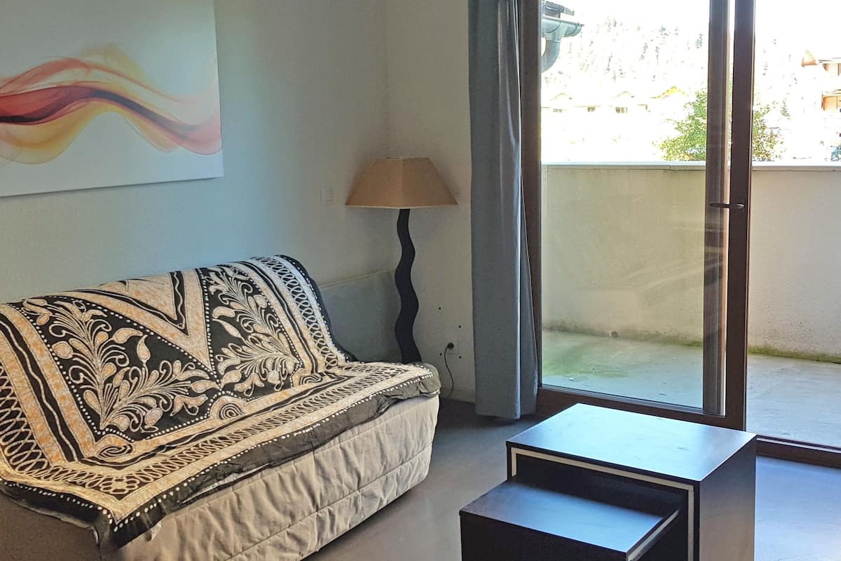 A living room with a patterned sofa, a lamp, and a view through a sliding door to an outdoor area.