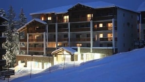 A multi-story hotel with balconies, snow-covered surroundings, and warm lighting. - Résidence Les Blanches Provençales (Selonnet)