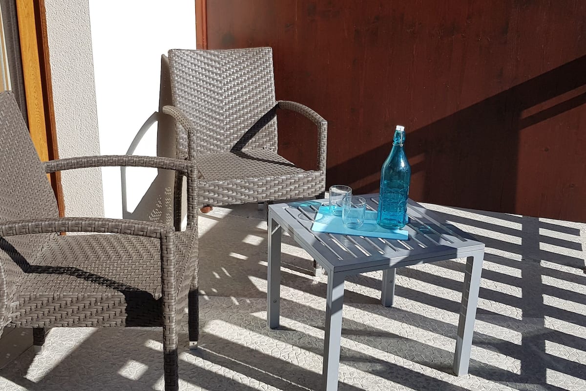 A wicker chair and a metal table with a bottle and glasses on it.
