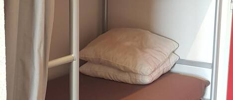A bunk bed with a single pillow on the lower bunk.