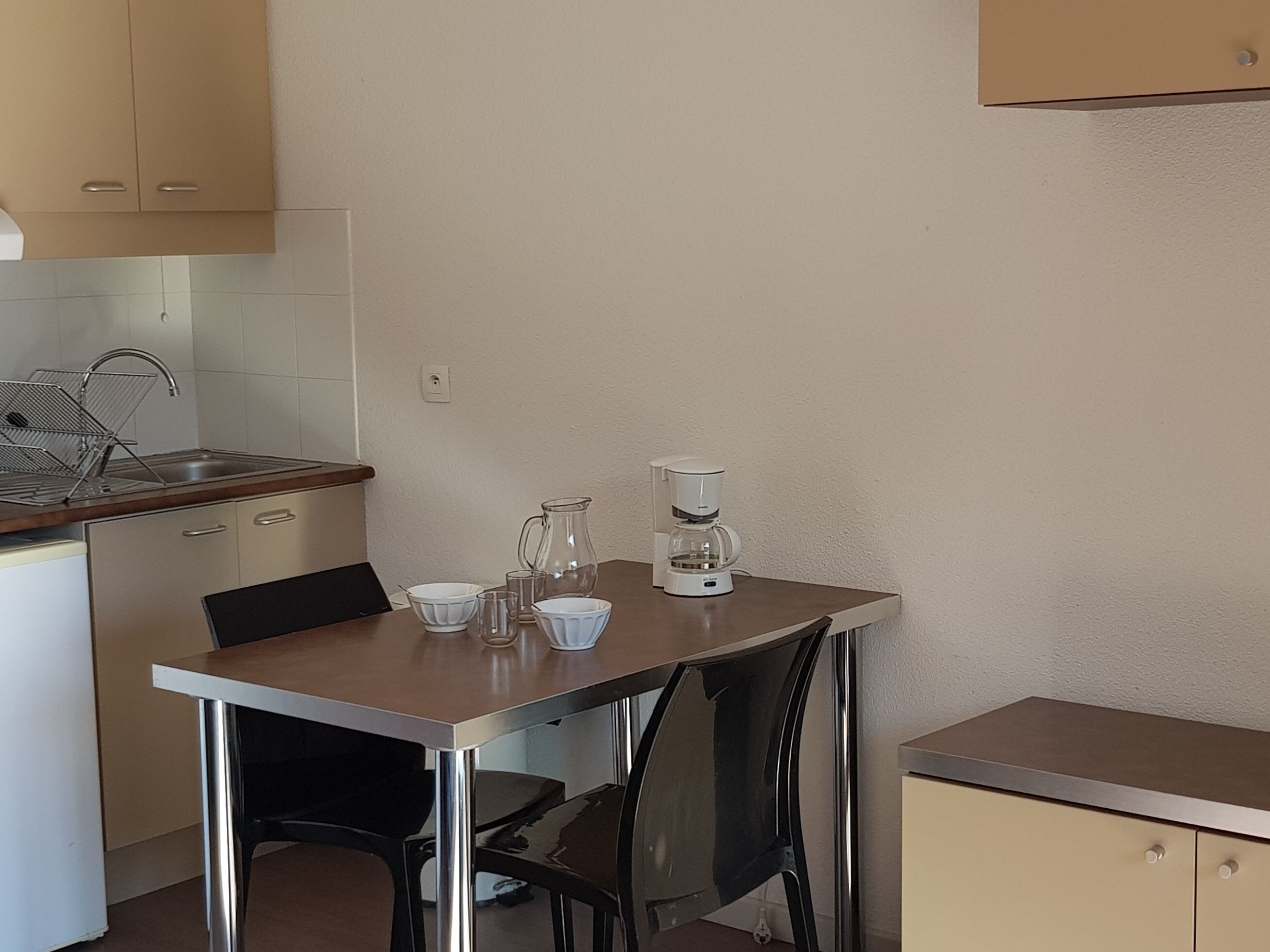 A compact kitchen with a sink, a coffee maker, and a dining table with chairs.