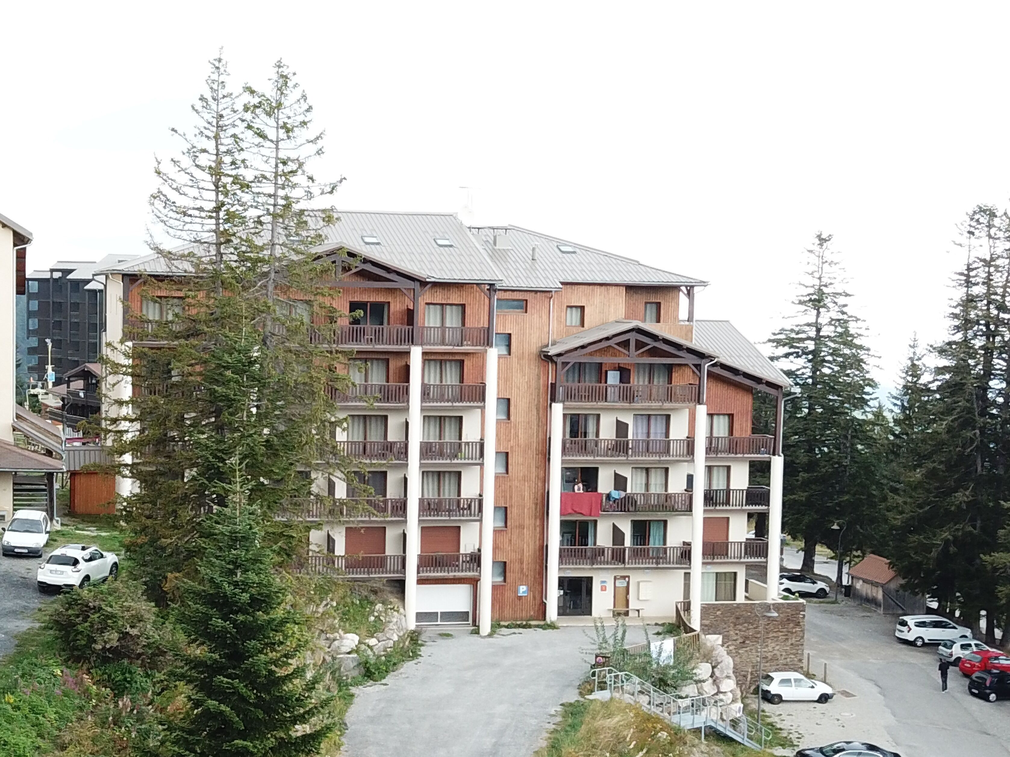 Un hotel de varios pisos con balcones, un estacionamiento y árboles circundantes.