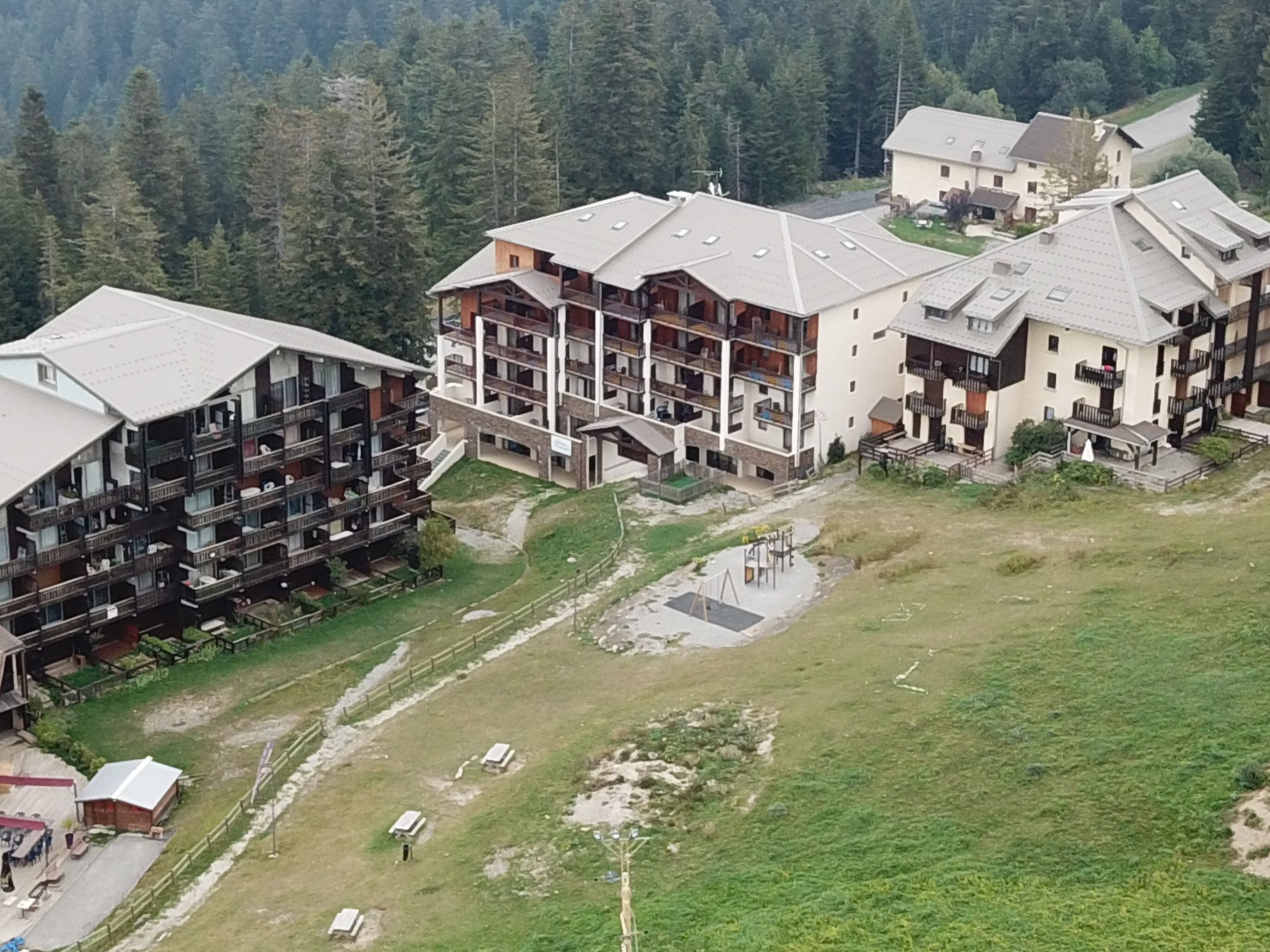 A multi-story hotel with balconies, a grassy courtyard, and a forested backdrop.