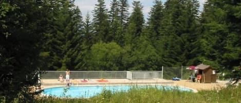A swimming pool surrounded by a metal fence, with a small wooden structure nearby.