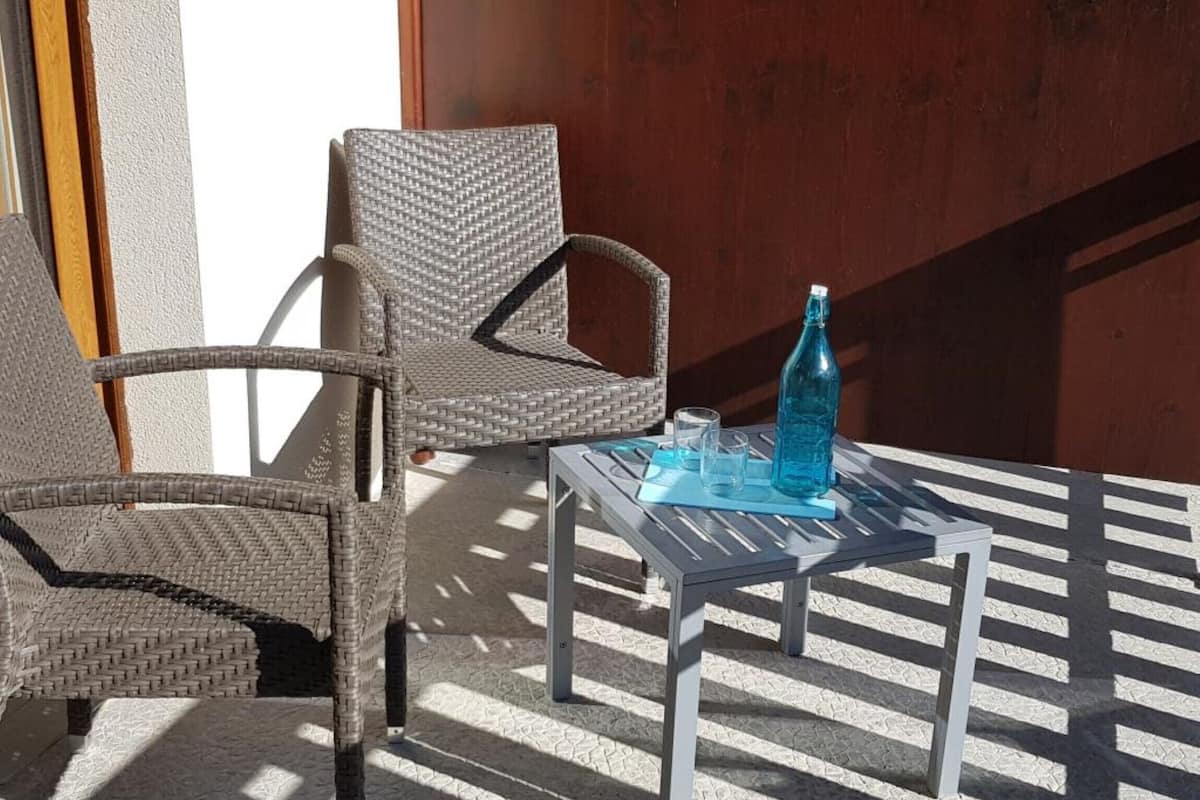 A wicker chair and a table with a bottle and glasses on it.