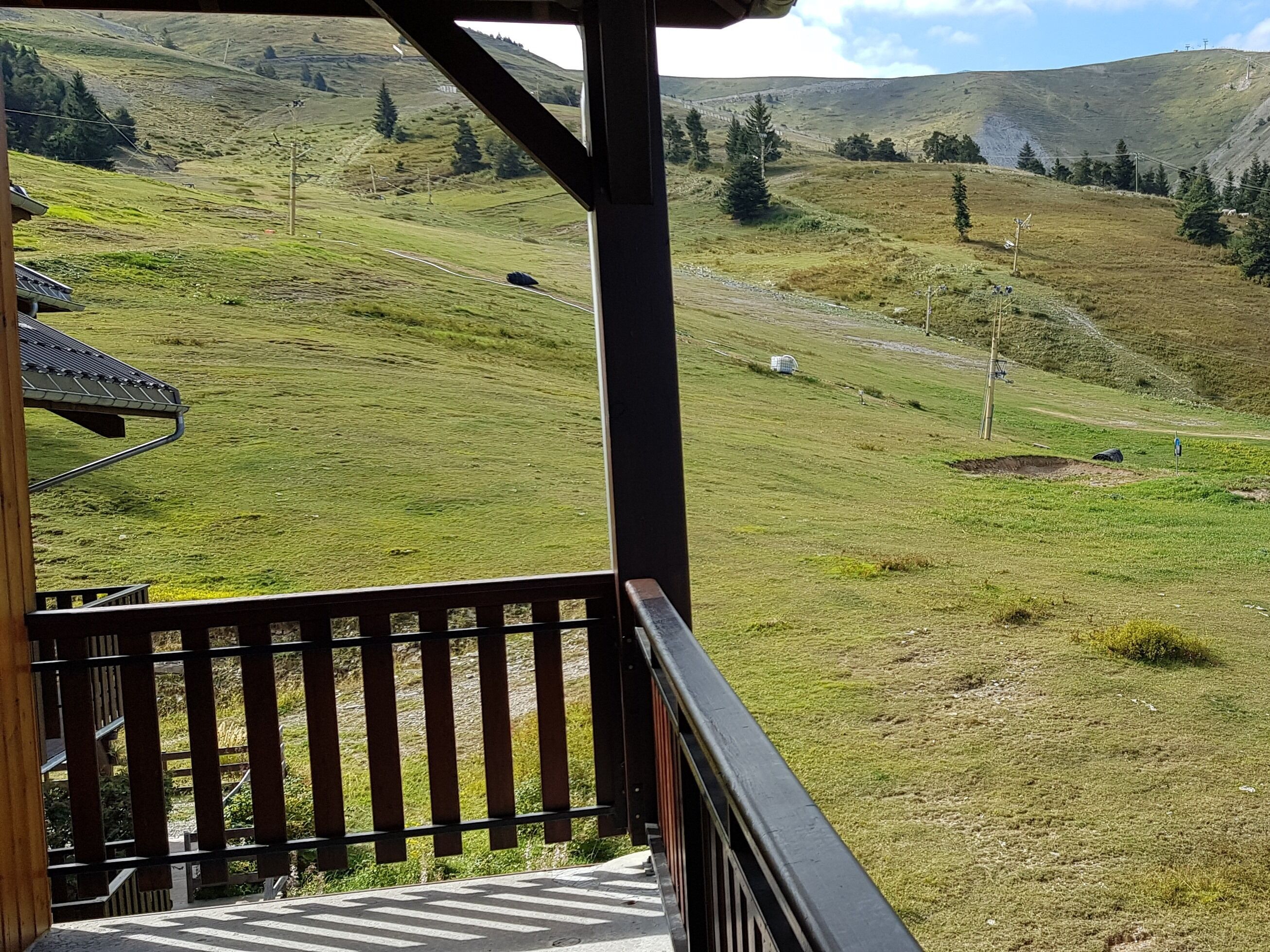 Een balkon met uitzicht op een groene heuvel, een houten constructie en een metalen reling.