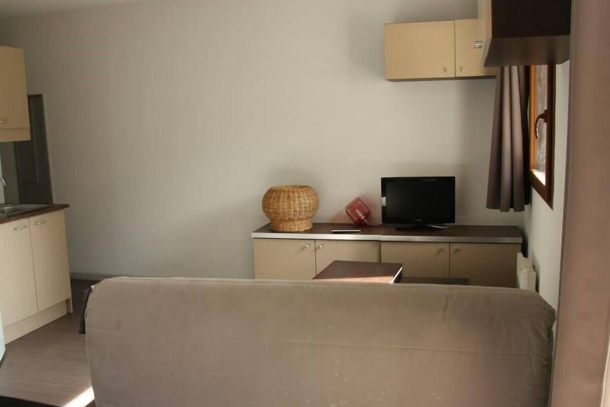A small, compact living space with a kitchenette, a sofa, a television, and a cabinet.