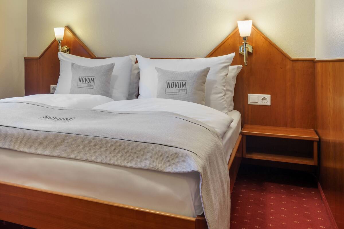 A neatly made bed with a white bedspread and pillows, a wooden headboard, and bedside lamps.