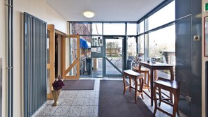 A modern hotel lobby with a glass door entrance, a reception desk, and a seating area with wooden chairs and tables.