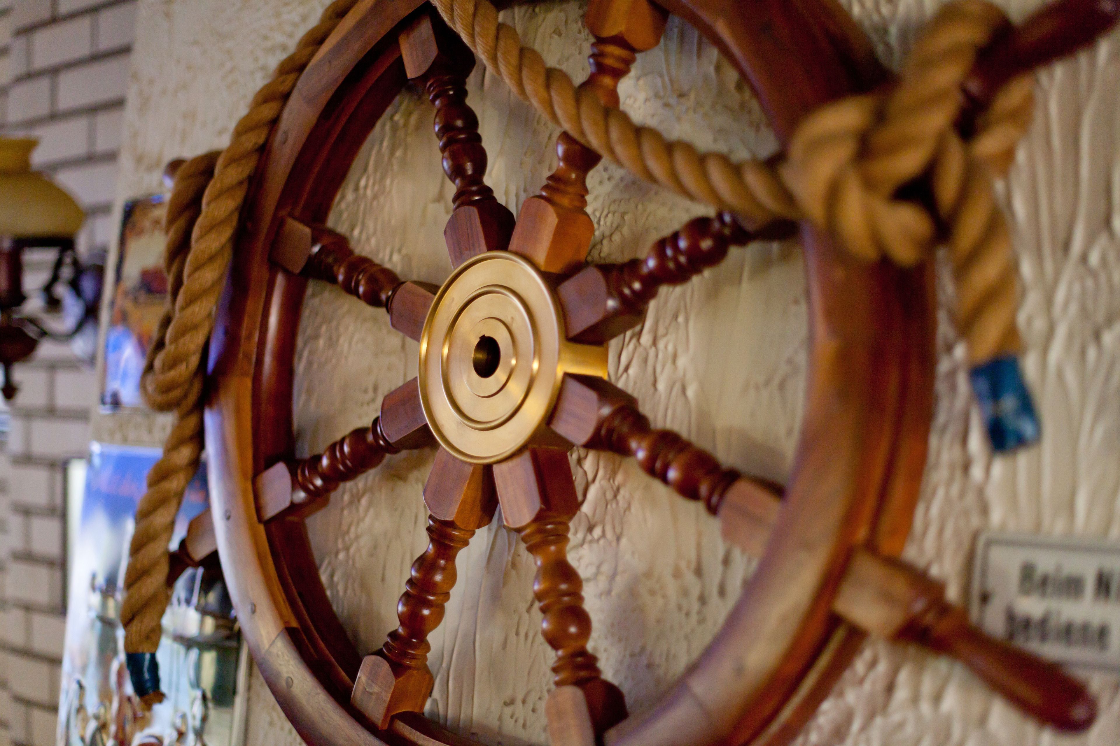 A wooden ship's wheel with a rope wrapped around it, mounted on a textured wall.