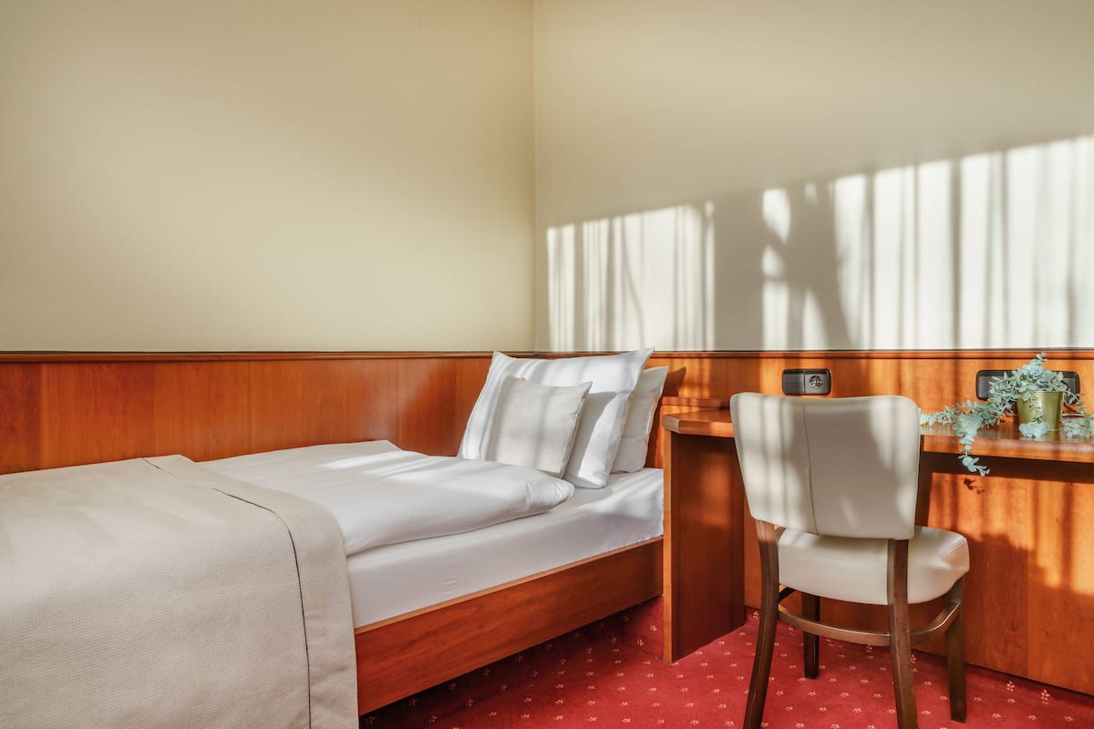 A hotel room with a wooden bed, a desk with a chair, and a window with curtains.