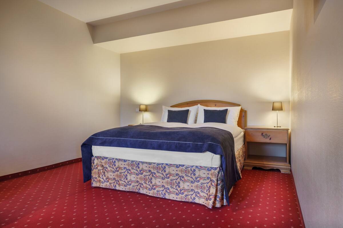 A neatly made bed with a blue and white bedspread, two bedside lamps, and a wooden nightstand with a drawer.