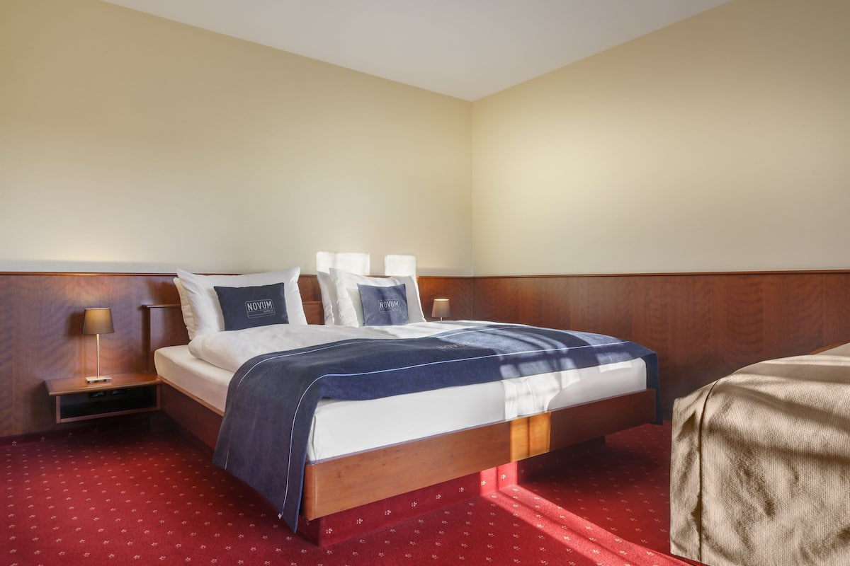 A hotel room with a bed, bedside tables, and a red carpet.