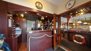 A wooden reception desk with a lifebuoy, a clock, and a maritime-themed wall decoration.