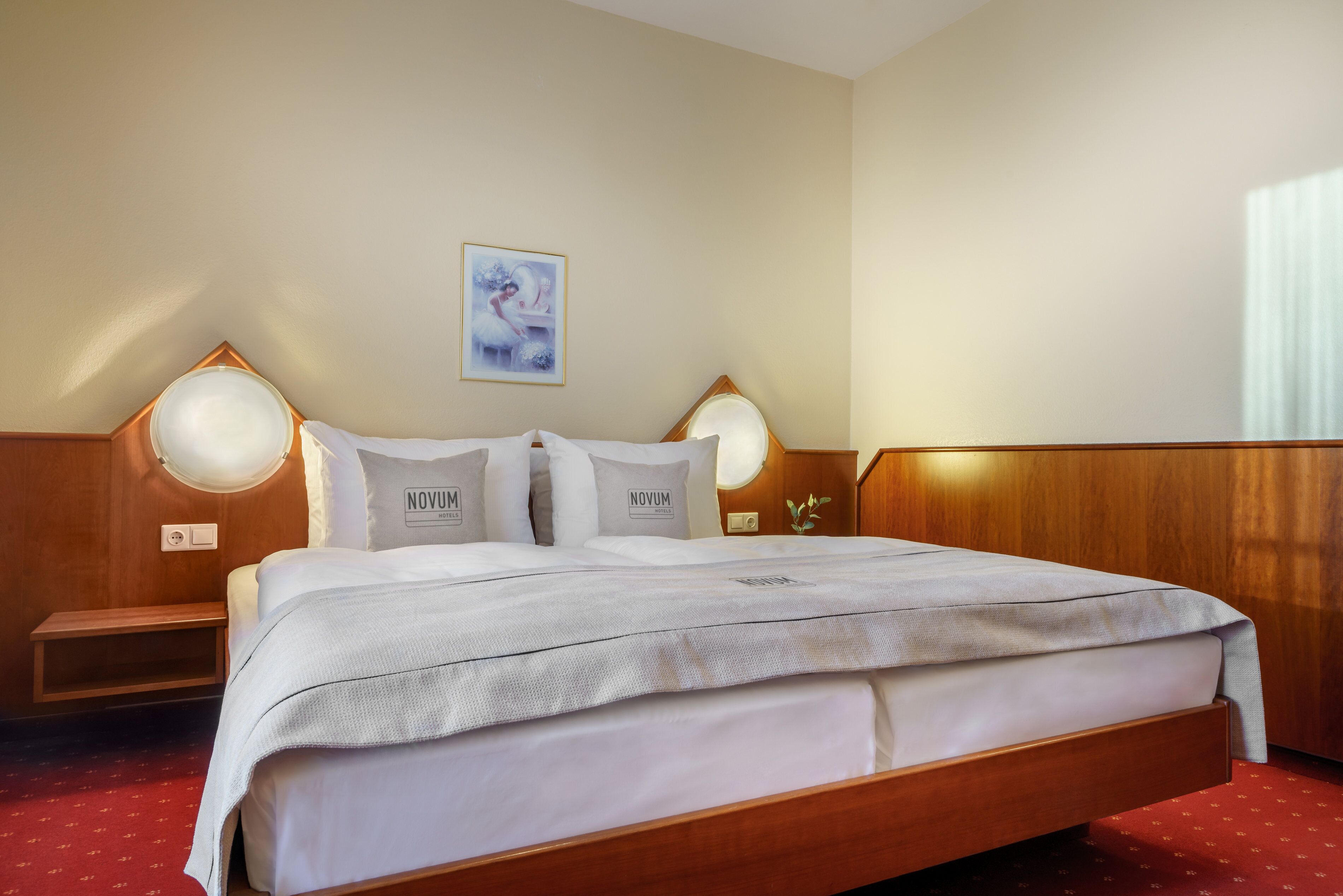 A hotel room with a large bed, two bedside tables, a nightstand, a wall-mounted lamp, and a framed picture on the wall.