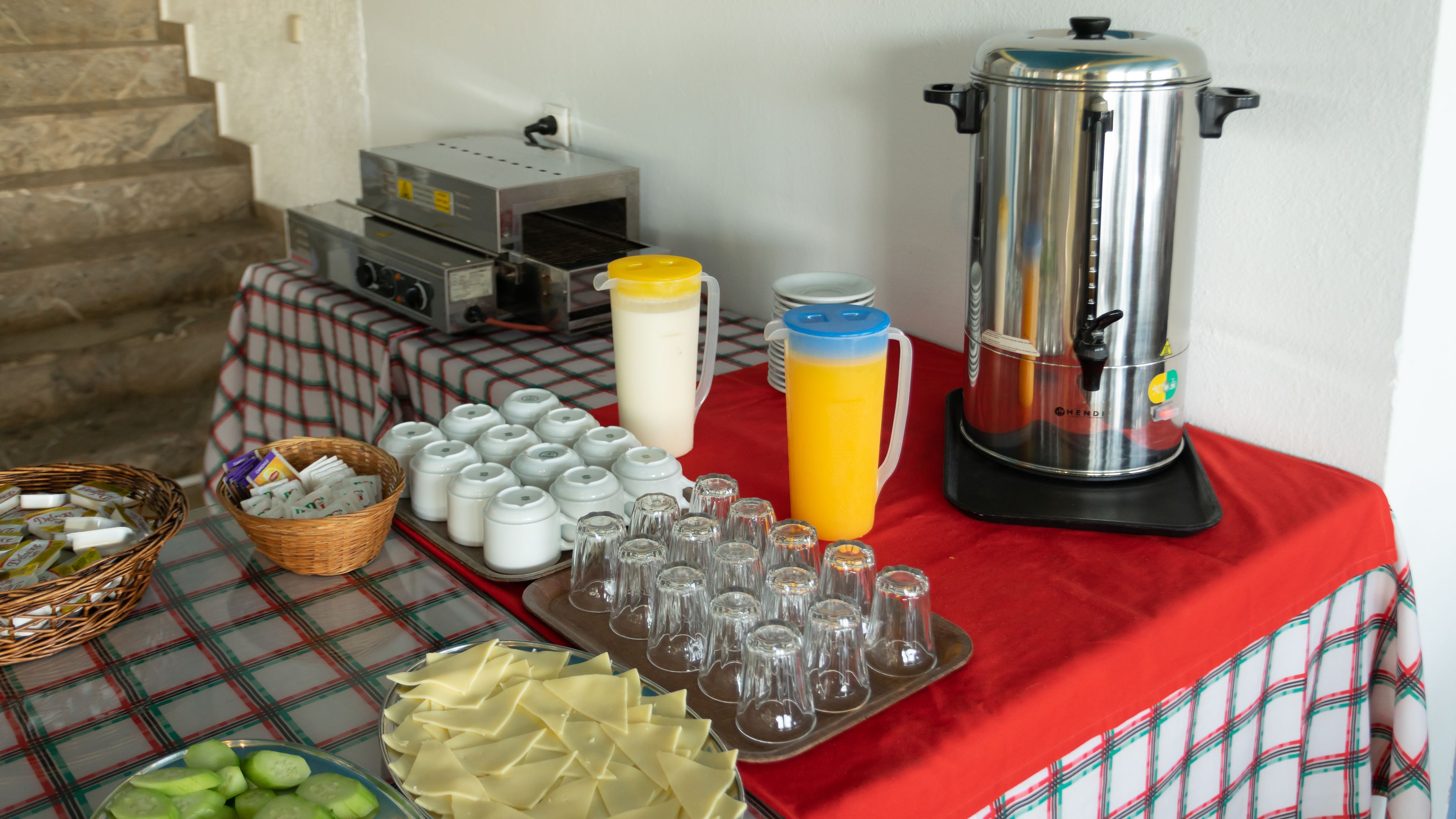 A buffet table with various food items, a coffee maker, and a juice dispenser.
