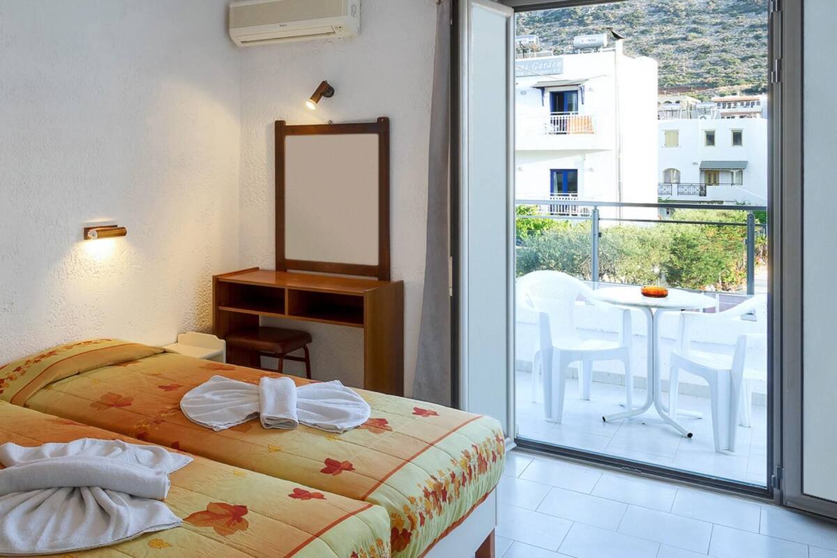 A hotel room with two beds, a large window, and a balcony with outdoor seating.