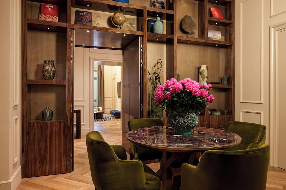 Un comedor con una mesa redonda, cuatro sillas verdes y un jarrón de flores rosadas.