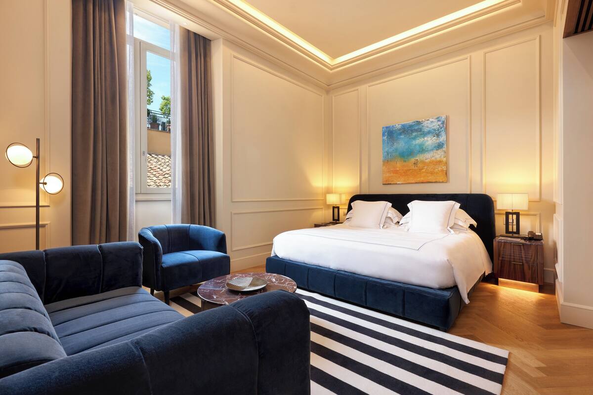 A hotel room with a large bed, two armchairs, a coffee table, and a painting on the wall.