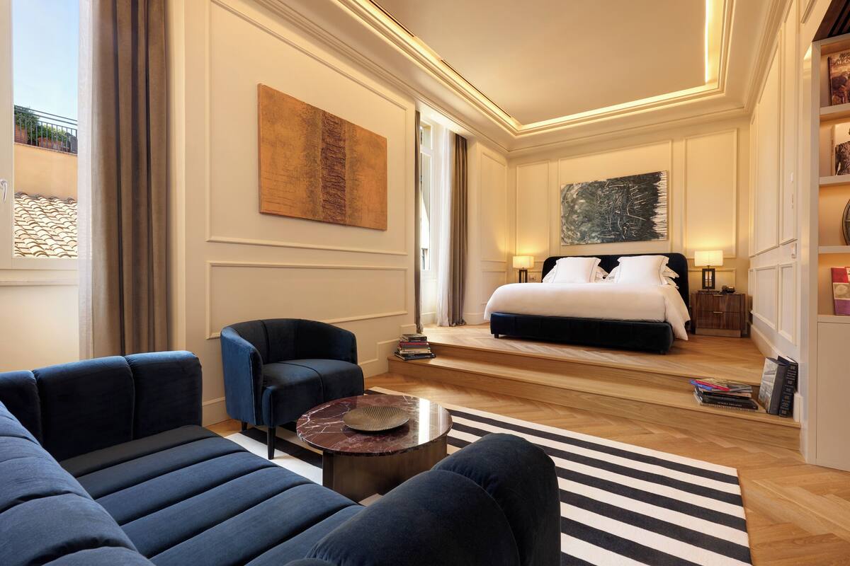 A modern hotel room with a large bed, a sofa, a coffee table, and a striped rug.