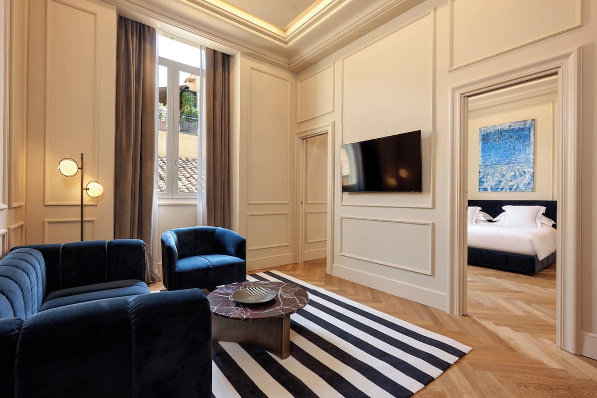 A modern hotel room with a large bed, a TV mounted on the wall, and a seating area with two sofas and a coffee table.
