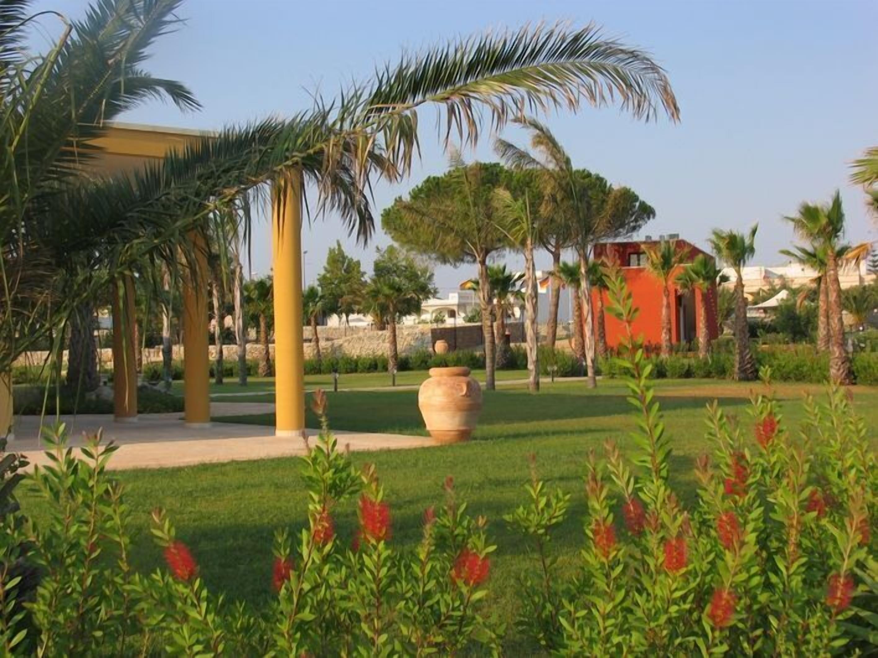 A landscaped garden with palm trees, a large planter, and a building with a red facade.