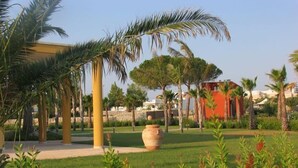 Un jardín ajardinado con palmeras, una jardinera grande y un edificio de fachada roja.