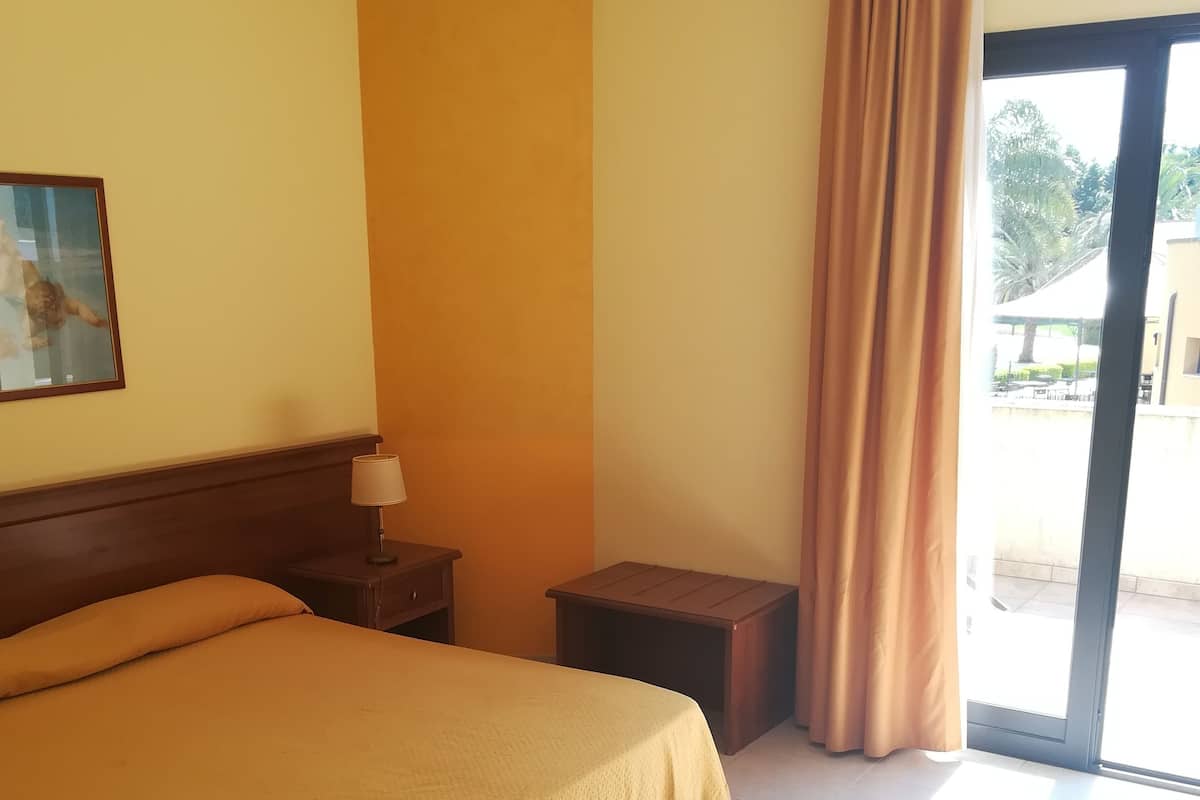 A hotel room with a large bed, a nightstand, a lamp, a small table, and a window with curtains.