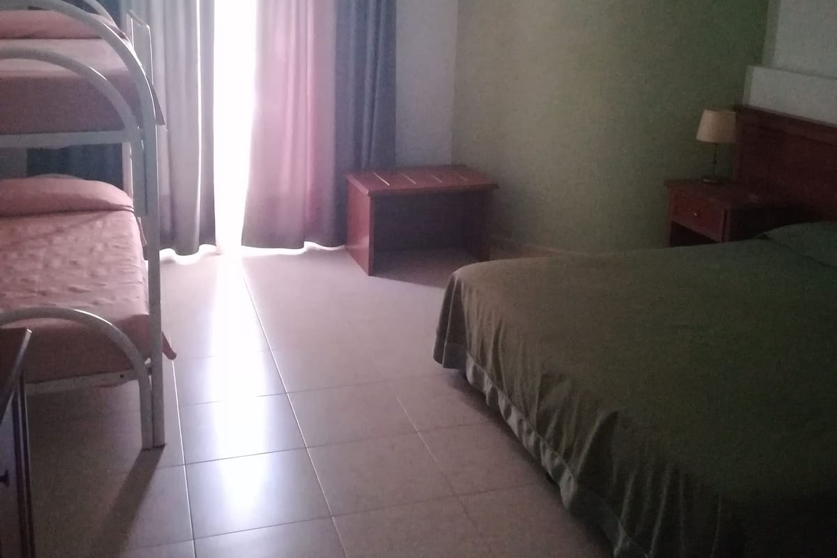 A hotel room with bunk beds, a bedside table, a lamp, and a window with curtains.