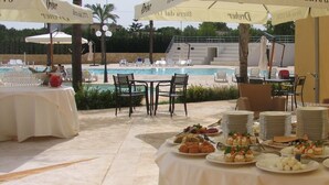 Un área de comedor al aire libre con mesas, sillas y una piscina al fondo.