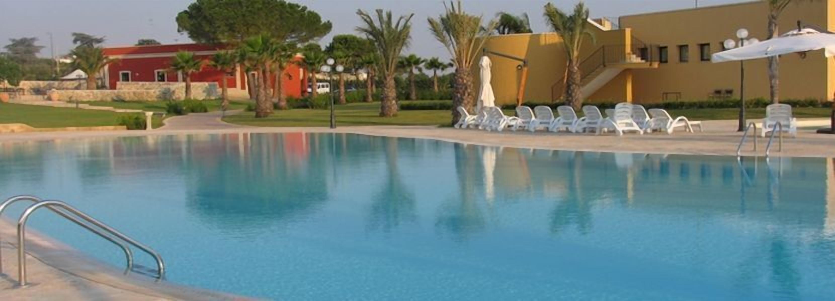 A swimming pool with clear blue water, surrounded by white lounge chairs and palm trees.