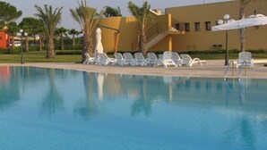 Una piscina con agua cristalina azul, rodeada de sillas de descanso blancas y palmeras.
