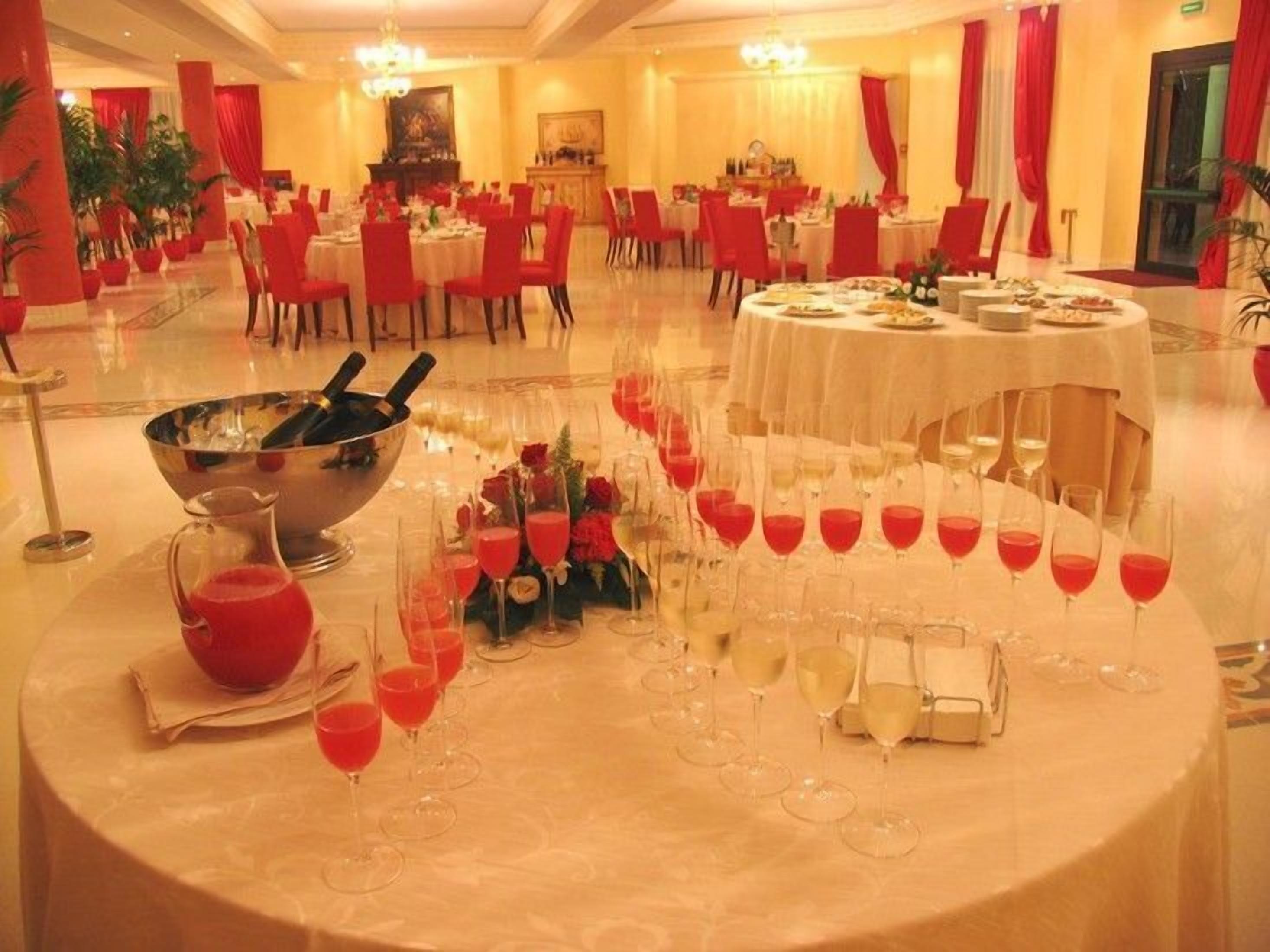 A banquet hall with round tables set for dining, a central bar area, and red curtains.