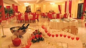 Un salón de banquetes con mesas redondas dispuestas para comer, una zona de bar central y cortinas rojas.