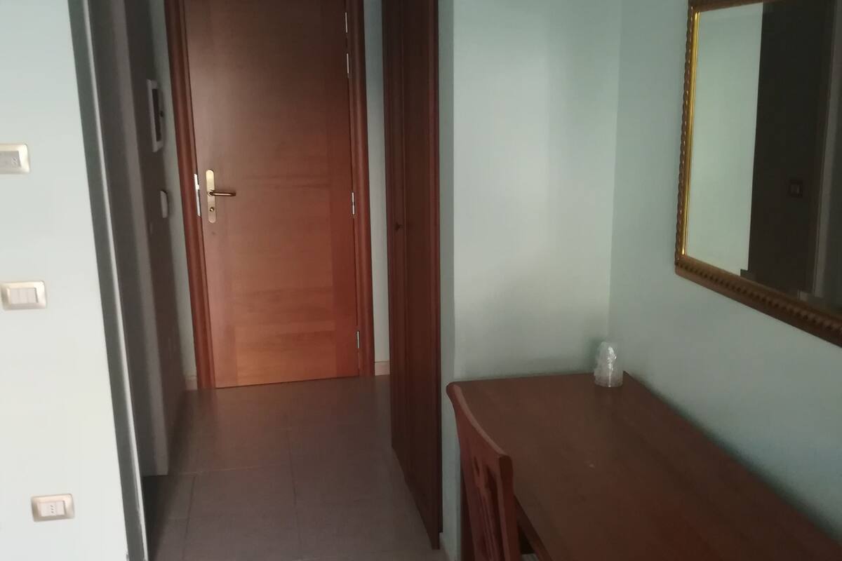 A hallway with a wooden door at the end, a wooden bench, and a mirror on the wall.