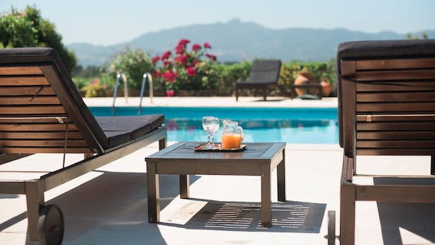 Zona de piscina con sillas de descanso y una mesa con un vaso y una jarra de jugo de naranja.