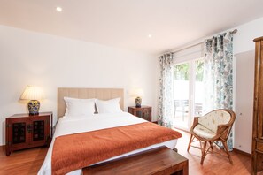 A hotel room with a large bed, two bedside tables with lamps, a wicker chair, and a view of the outdoors through a sliding glass door. - Quinta Verde Sintra (Sintra)
