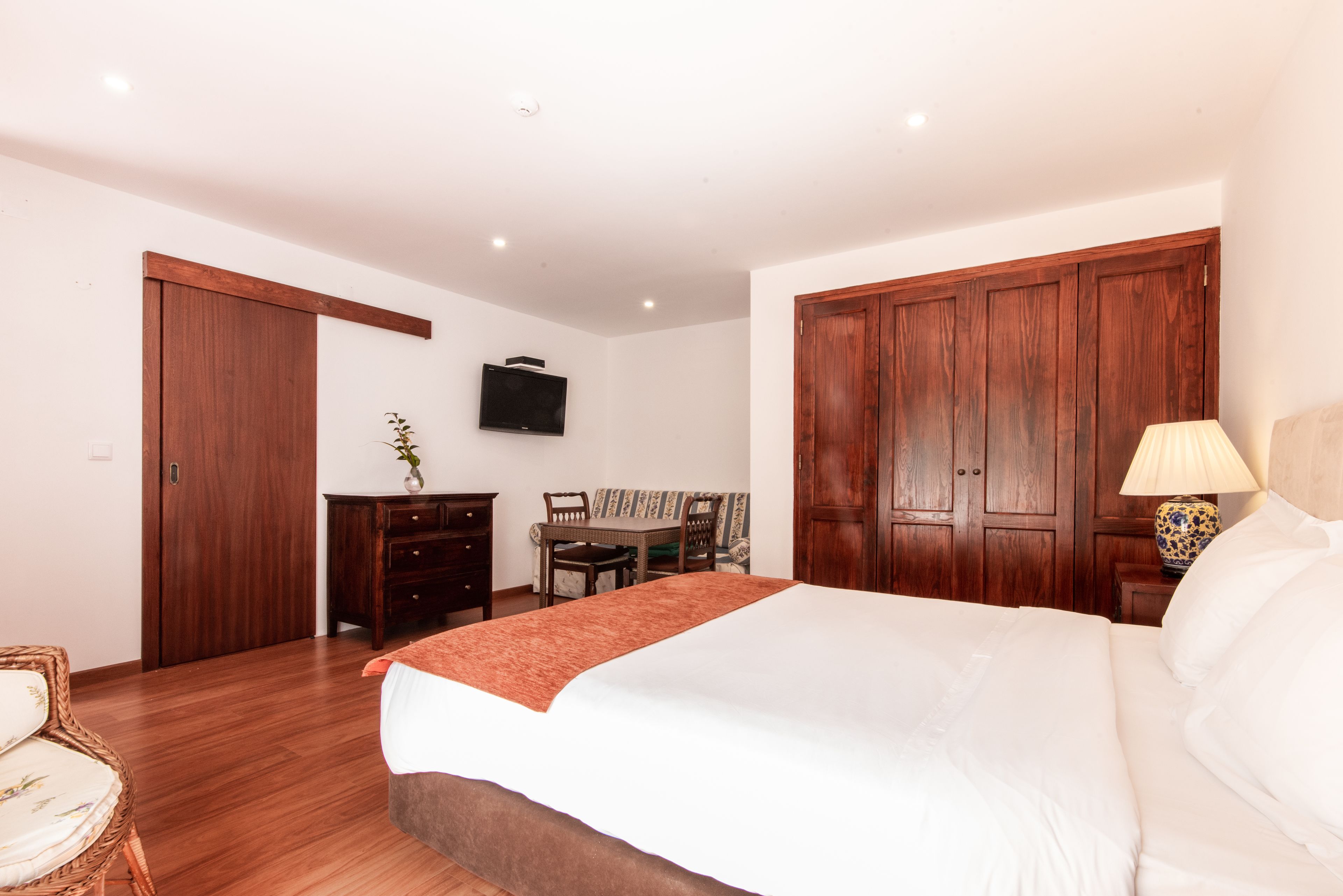 Ein Schlafzimmer mit einem großen Bett, einem Holzschrank, einem Fernseher, einem Schreibtisch und einem Sessel.