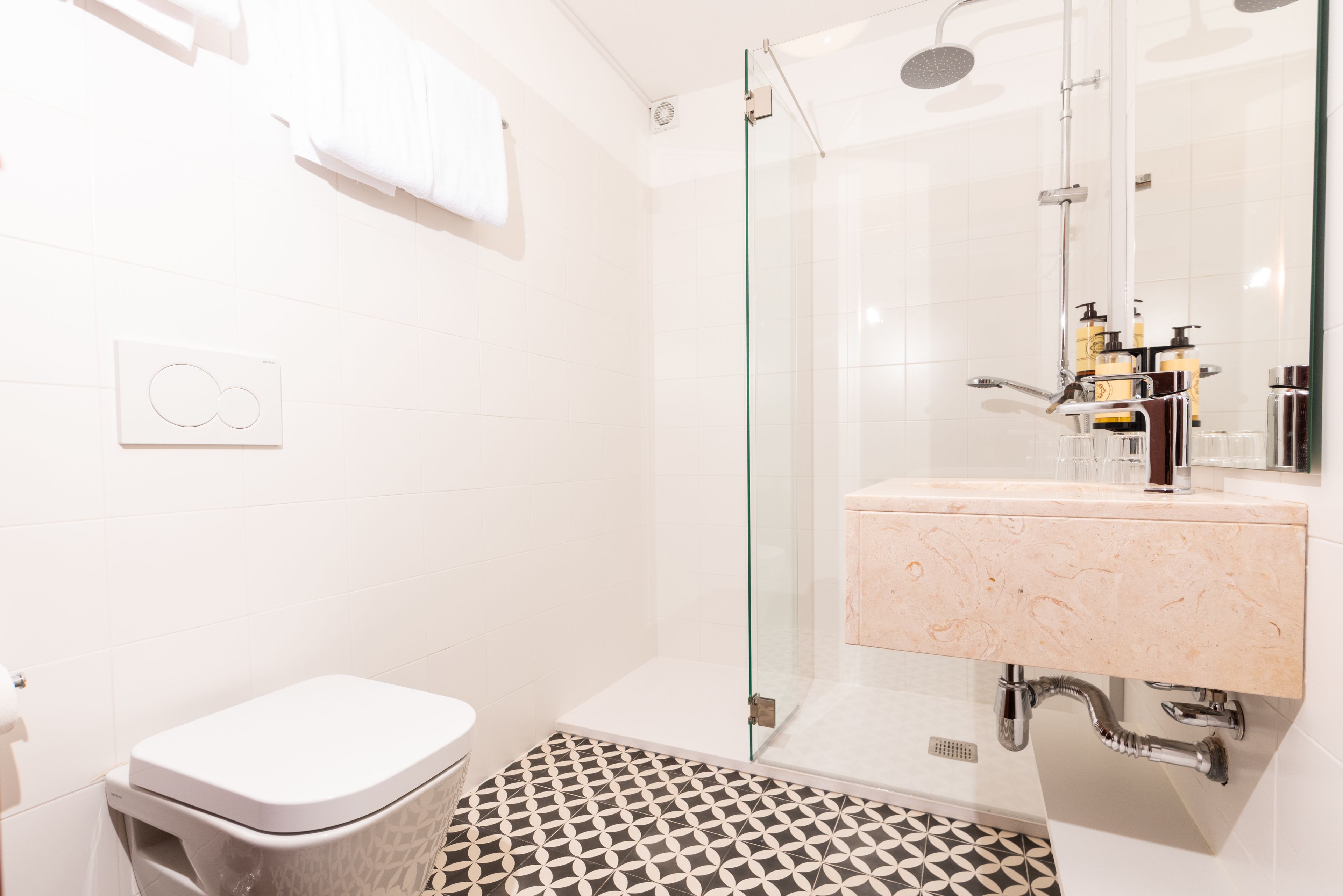 Un baño moderno con ducha envuelta en vidrio, inodoro blanco y lavamanos con encimera de mármol.