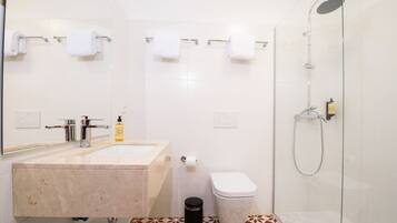 A modern bathroom with a marble sink, a toilet, and a glass-enclosed shower.