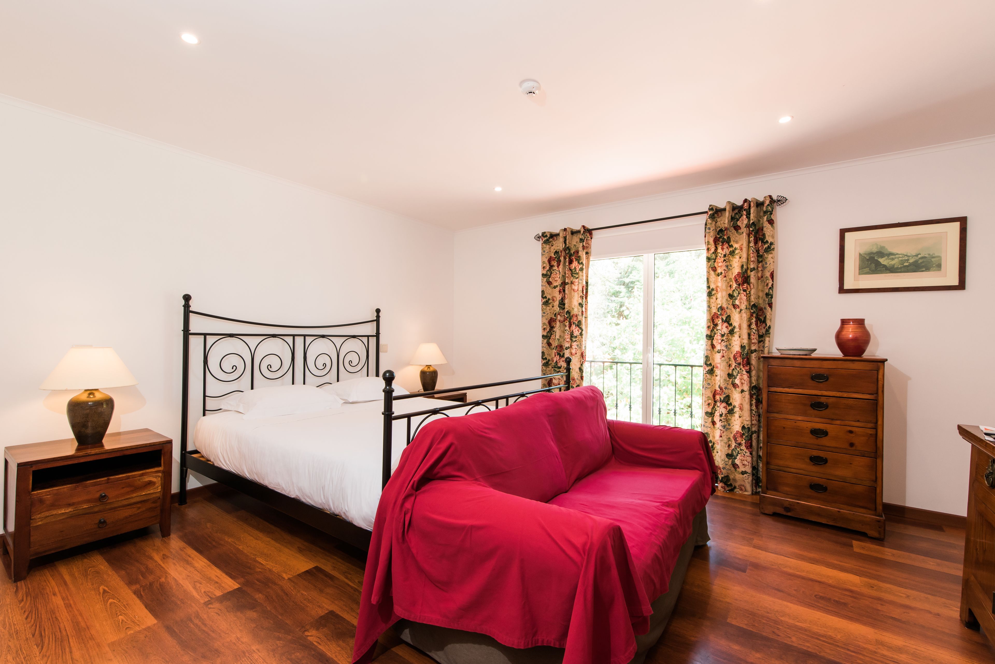 A bedroom with a bed, a nightstand with a lamp, a dresser, and a window with curtains.