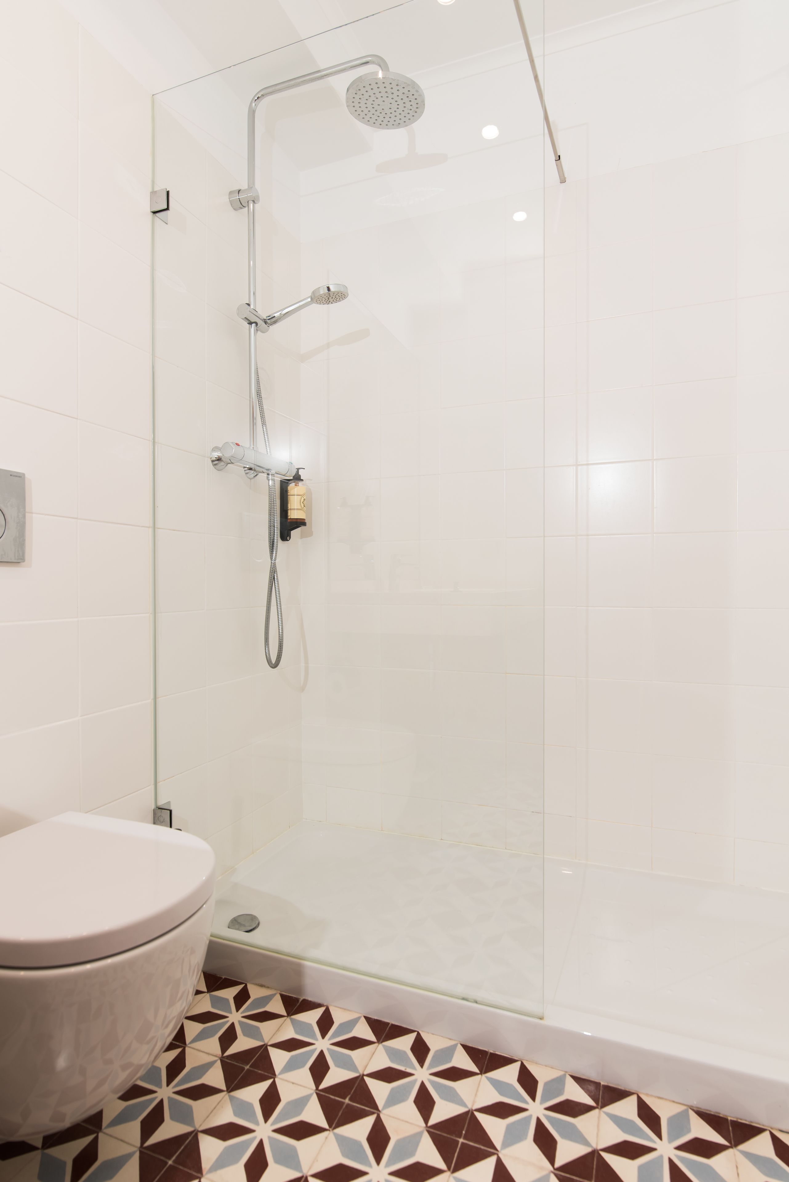 Un baño moderno con cabina de ducha de vidrio, inodoro y baldosas de suelo estampadas.
