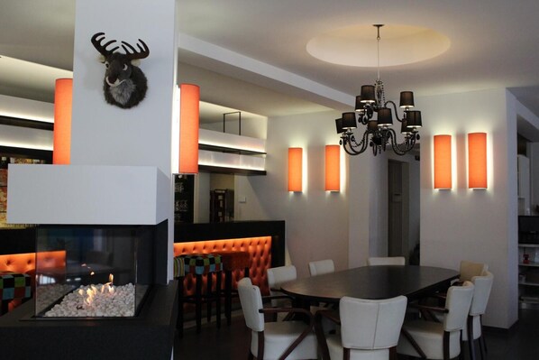 A modern dining area with a fireplace, a chandelier, and orange wall sconces.