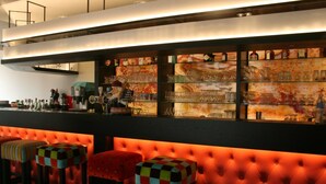 A bar area with a red upholstered bar counter and colorful stools. - Hotel La Terrasse (De Panne)