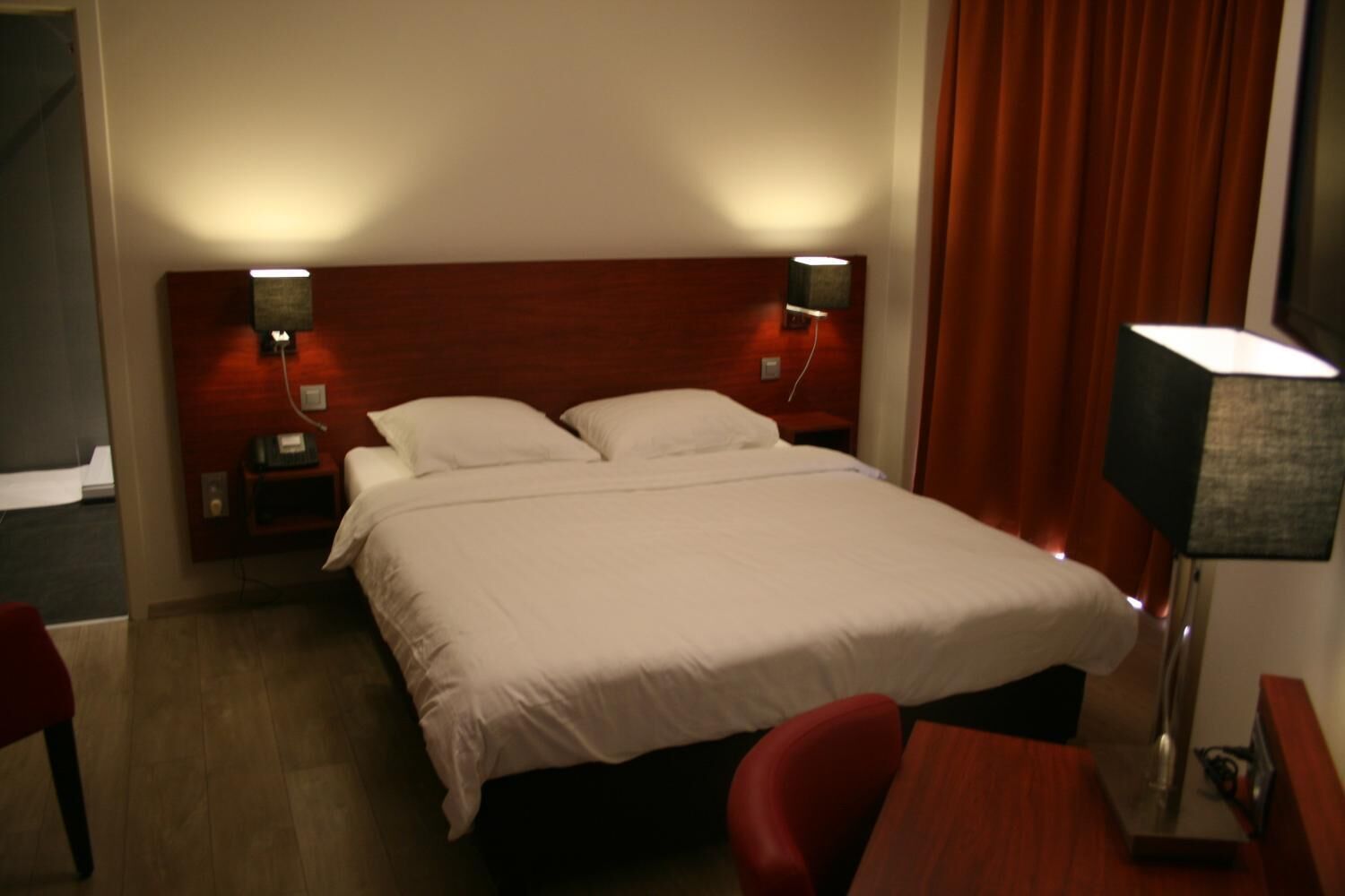 Una habitación de hotel con una cama grande, dos mesitas de noche con lámparas, un escritorio con una silla y una ventana con cortinas.